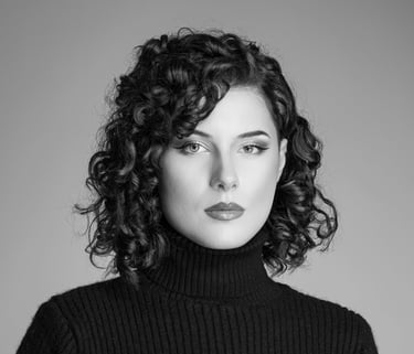  Ein Schwarz-Weiß-Porträt einer Frau mit kurzen, lockigen Haaren. Sie trägt einen dunklen Rollkragenpullover und hat einen au