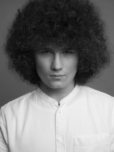 Schwarz-Weiß-Porträt eines jungen Mannes mit voluminösem Afrohaar und weißem Hemd.