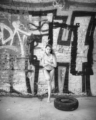 Schwarz-Weiß-Portrait einer Frau in Unterwäsche vor einer Graffiti-Backsteinwand, urban und künstlerisch inszeniert – LensAnd