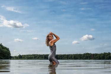 Eine Frau in einem nassen silbernen Kleid steht im See und posiert vor einem bewölkten Himmel.