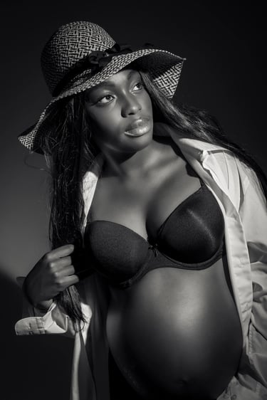 Stilvolles Babybauchshooting in Schwarz-Weiß – werdende Mutter mit Hut, offenem weißen Hemd und BH im dramatischen Licht. Sch