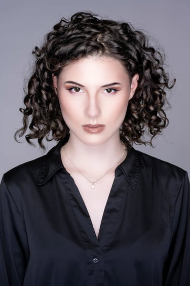 Studio-Porträt einer jungen Frau mit lockigem Haar und elegantem Ausdruck, aufgenommen von LensAndLook – klarer, moderner Loo