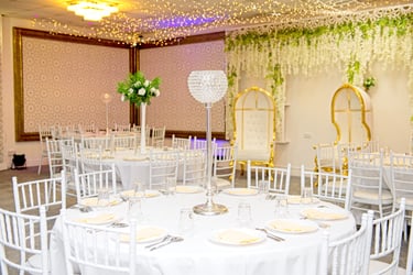 nside wedding venue, white round table, white chairs, crystal centrepiece, fairy lights on ceiling