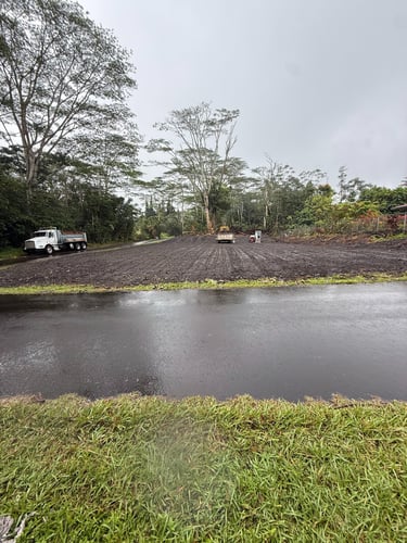 White dump truck and heavy excavation machinery leveling a dirt construction site near a paved road.