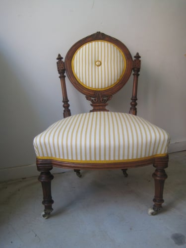 Antique nursing chair with traditional upholstered seat and back, with a white and yellow striped fabric