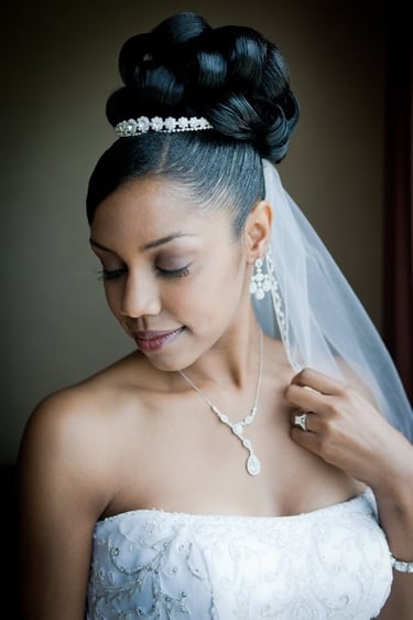 Black bride with elegant bridal updo of large curls, jeweled headband, veil, strapless gown, and natural soft wedding makeup.