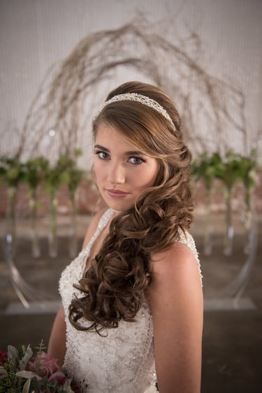 Bride with brown hair in half-up half-down hairstyle, soft curls, jeweled headband, and natural makeup with long lashes.