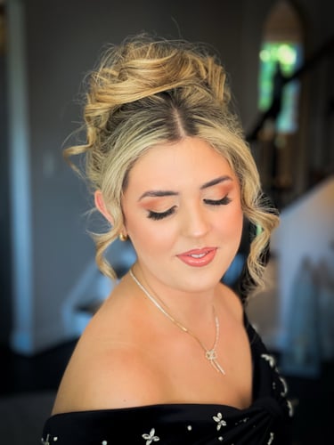 Bride with blonde hair styled in an elegant updo, soft-glam wedding makeup, long lashes, peach lips, and off-shoulder gown.