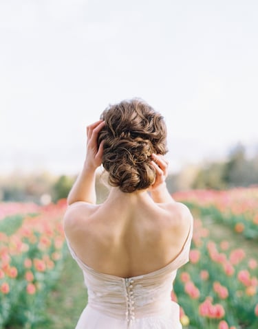 A brunette bride standing in a field of flowers, displaying her updo hairstyle.