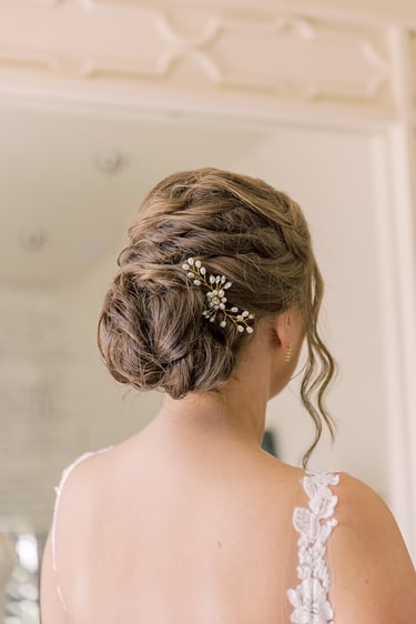 Brunette bride with woven bridal updo hairstyle, pearl floral hairpiece, and soft curls, styled elegantly for her wedding.