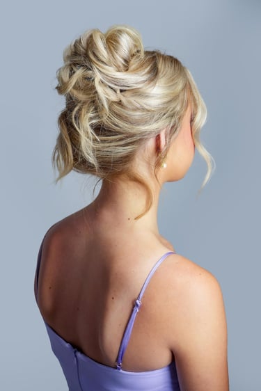 Blonde bride with textured messy updo, soft curls, and loose tendrils, styled for elegant bridal or bridesmaid look.