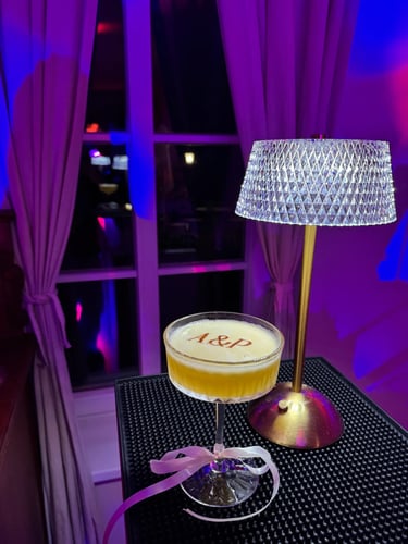 A personalized foam cocktail with A&P monogram initials next to a crystal table lamp in a purple lit lounge.