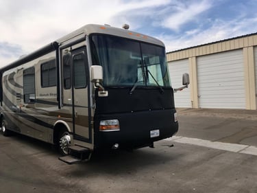 A Newmar Dutch Star Class A motorhome with a black protective front bra mask parked near storage units.