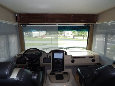 Interior view of a modern Class A motorhome cockpit featuring a dashboard, steering wheel, and leather pilot seats.