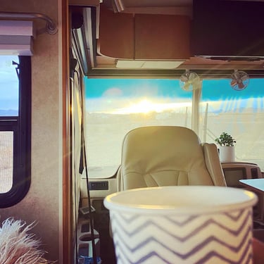 Sunset view through an RV windshield with a coffee cup in the foreground of the motorhome interior.