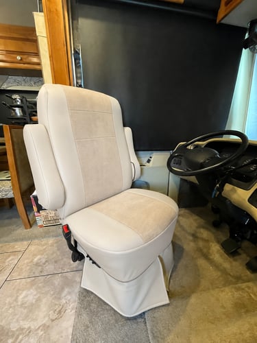 Swivel beige leather RV captain's chair inside a motorhome cockpit with a steering wheel.