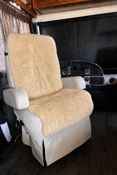 A tan sheepskin seat cover on a white leather RV captain chair in a motorhome cockpit.