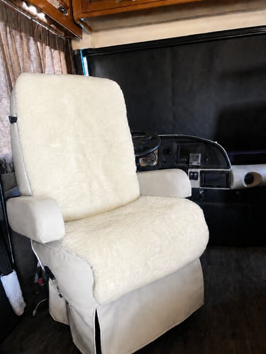 A plush white sheepskin seat cover installed on a leather RV captain's chair inside a motorhome cockpit.