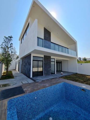 Fachada posterior de casa moderna de dos niveles con área de jardín y alberca