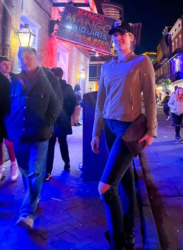 A tall woman posing on Bourbon Street at night near a neon Mango Mango Daiquiri sign.