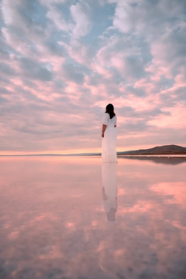 Woman in white dress standing in Tuz Gölü, Turkey, reflecting the pastel sky at sunset