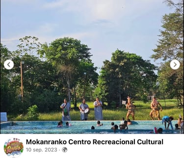 Indigenous performers dancing and drumming for people in a swimming pool at Mokanranko Centro Recreacional.