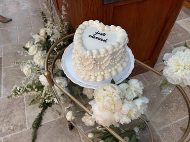 Heart-shaped vintage wedding cake with white frosting and 'just married' script on a gold cart.
