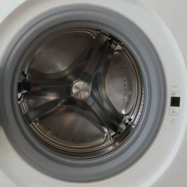 A close-up of a high-efficiency washing machine's drum being inspected by a professional in a Middle Eastern / Gulf apartment, soft lighting, clean and professional.