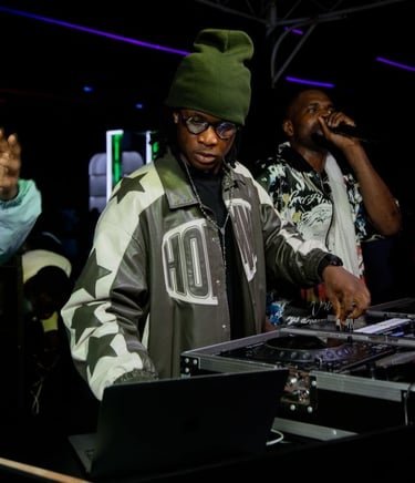 foto de um DJ e um cantor negros se apresentando em uma casa noturna, sob luzes roxas e verdes.