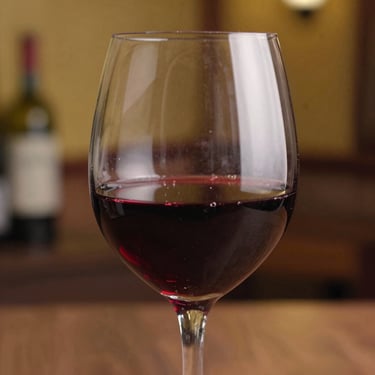 A crystal wine glass half-filled with red wine, capturing the reflection of a warm Western European interior.