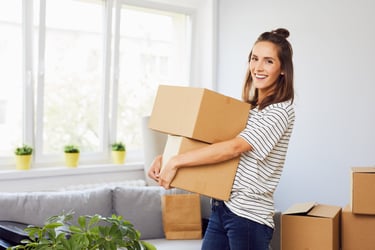 A female tenant holding cardboard moving boxes in her new bright living room