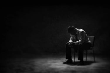 man seating on a chair, bent over his knees, in an empty room