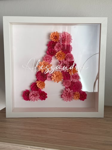 Quadro bianco,fatto a mano, con all'interno una lettera A composta da fiori di carta colorati vista frontale. 
