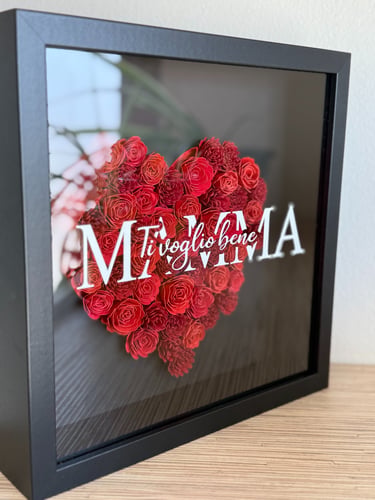 quadro nero  con un cuore rosso composto da fiori di carta realizzati a mano, sul vetro una scritta bianca vista laterale