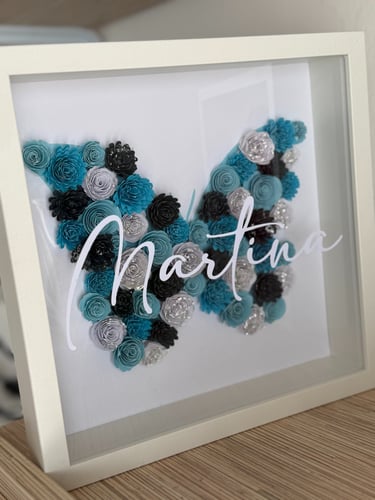 quadro bianco con farfalla di fiori assemblati all' interno sui toni dell'azzurro e il nome Martina bianco scritto sul vetro 