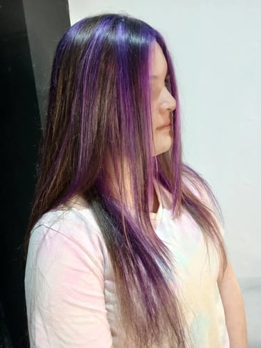 Woman showing off long brown hair with vibrant purple highlights and a money piece face frame.