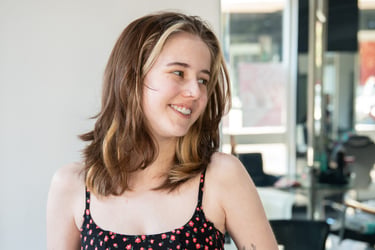 Smiling young woman with shoulder-length brown hair and blonde highlights in a floral dress.