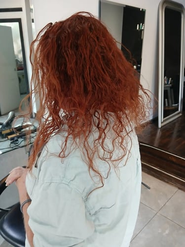 Back view of a person with vibrant long red hair sitting in a salon chair after a hair coloring treatment.