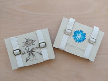 two large wooden flower presses with straps,one with andimage of a passion flower and one with an image of a cornflower