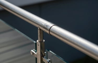 A detailed shot of polished stainless steel joints on a glass railing in a South American / Brazilian luxury apartment, showing precise craftsmanship and dark navy tones.