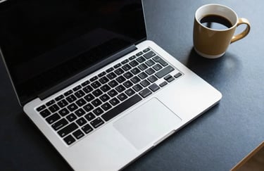 A minimalist overhead shot of a dark navy desk with a pale silver laptop and a gold tan coffee cup, suggesting focus.
