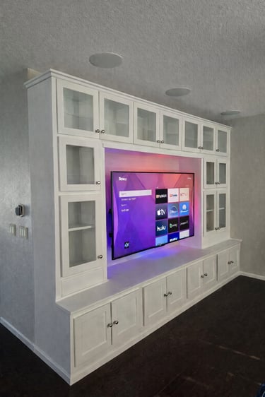 Custom white built-in entertainment center with glass cabinets and backlighting for a large Roku TV.