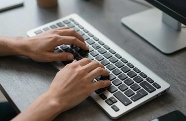 A bird's-eye view of a professional's hands typing on a high-end keyboard in a modern North American / US office, silver and charcoal tones.