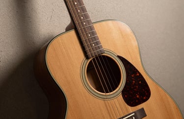A professional acoustic guitar with a rich bronze body and light oak neck, resting against a neutral textured wall.