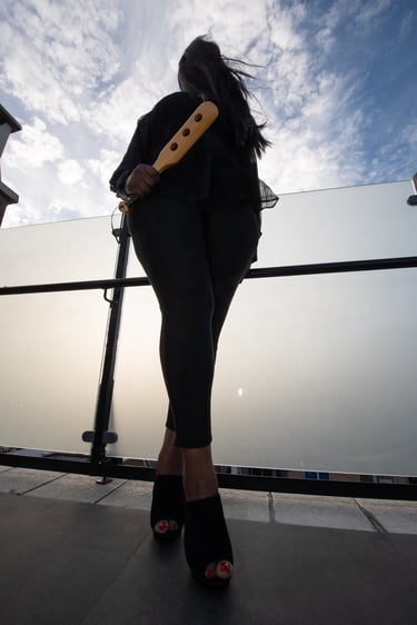 Teal Revel Cambridge Dominatrix holding a paddle