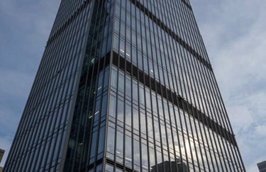 A wide-angle shot of a modern glass skyscraper reflecting a steel blue dusk sky. Mist white highlights on the sharp architectural lines.