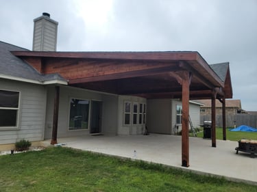Covered backyard patio with wooden beams and concrete flooring.