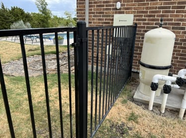 Black metal pool fence gate near filtration system.