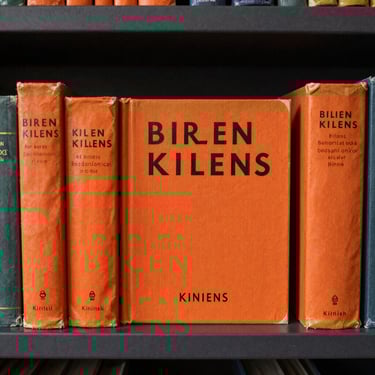 A collection of vintage children's books with vibrant burnt orange covers displayed on a dark charcoal shelf.