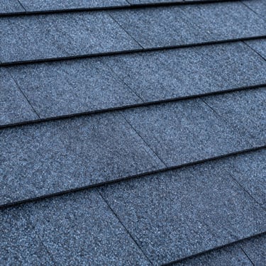 A close-up of high-quality, dark blue and grey architectural roofing shingles. Clean, professional North American / US construction material shot.